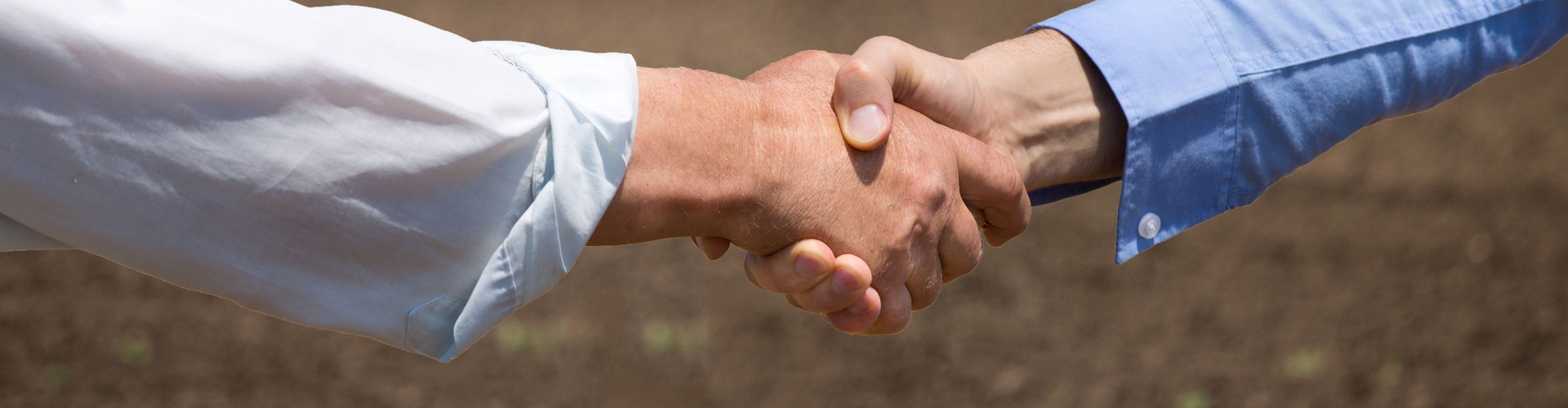 Zwei Personen, die sich die Hand reichen. Im Hintergrund fährt ein Trecker.